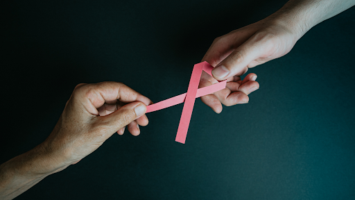 Two hands holding a pink ribbon.
